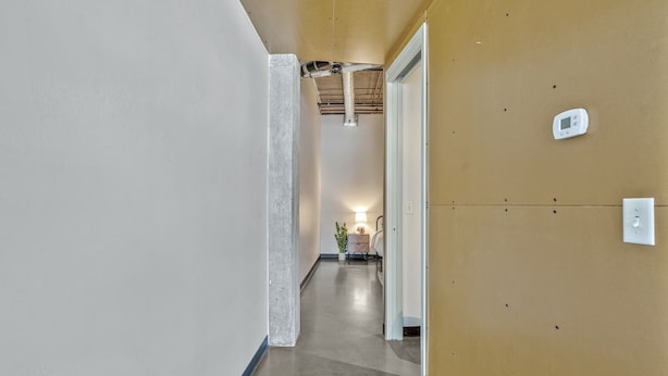 A hallway with a concrete floor, a light fixture, and a thermostat on the wall. - Chic Condo in The Gulch! (Nashville)