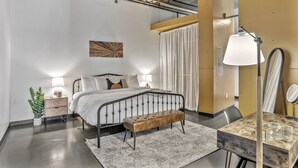 Une chambre à coucher moderne avec un cadre de lit en métal, un banc en bois, une table de chevet avec une lampe et un grand miroir.