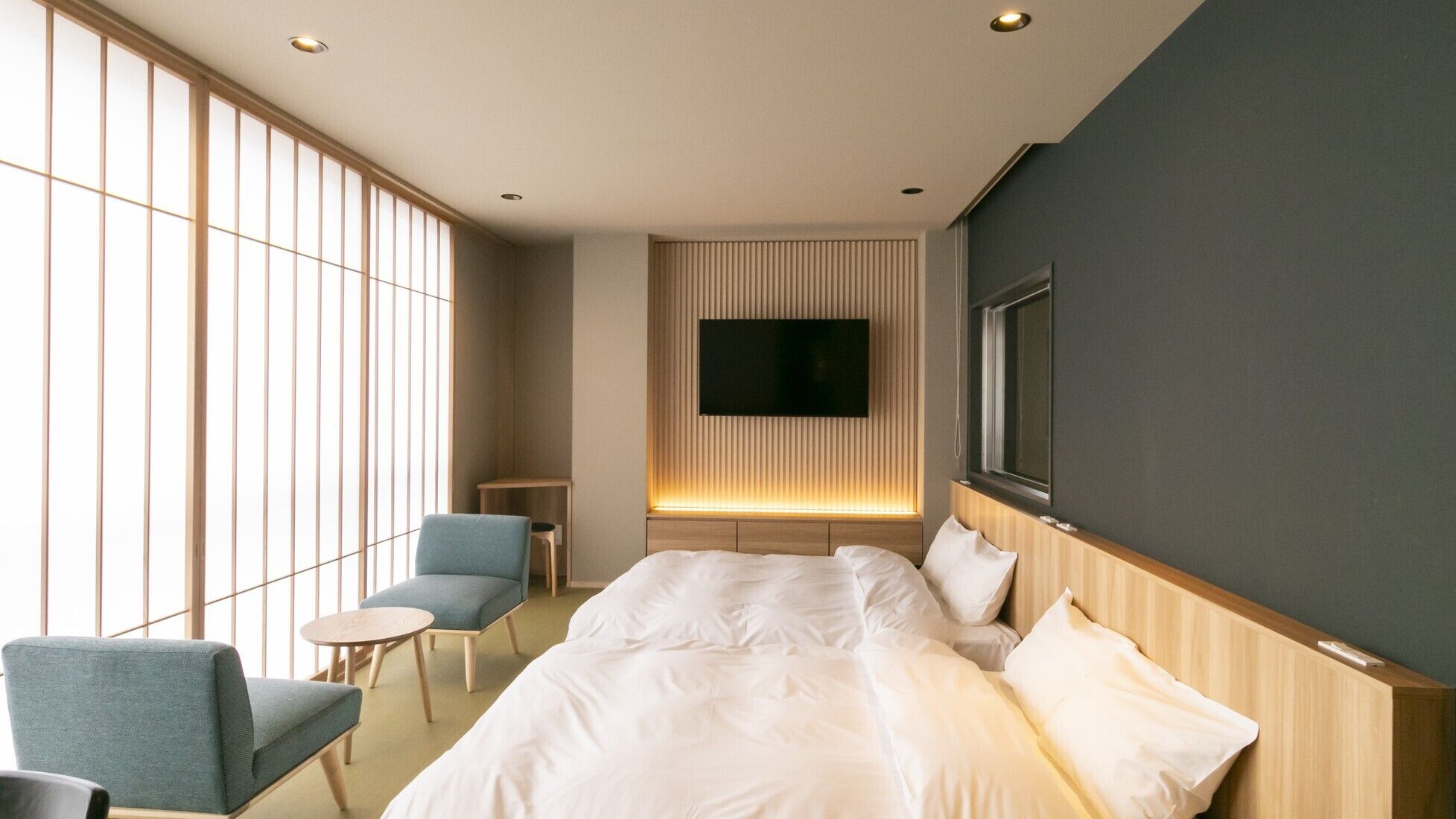 Ein Hotelzimmer mit Bett, Wandfernseher, Sessel und kleinem Tisch.