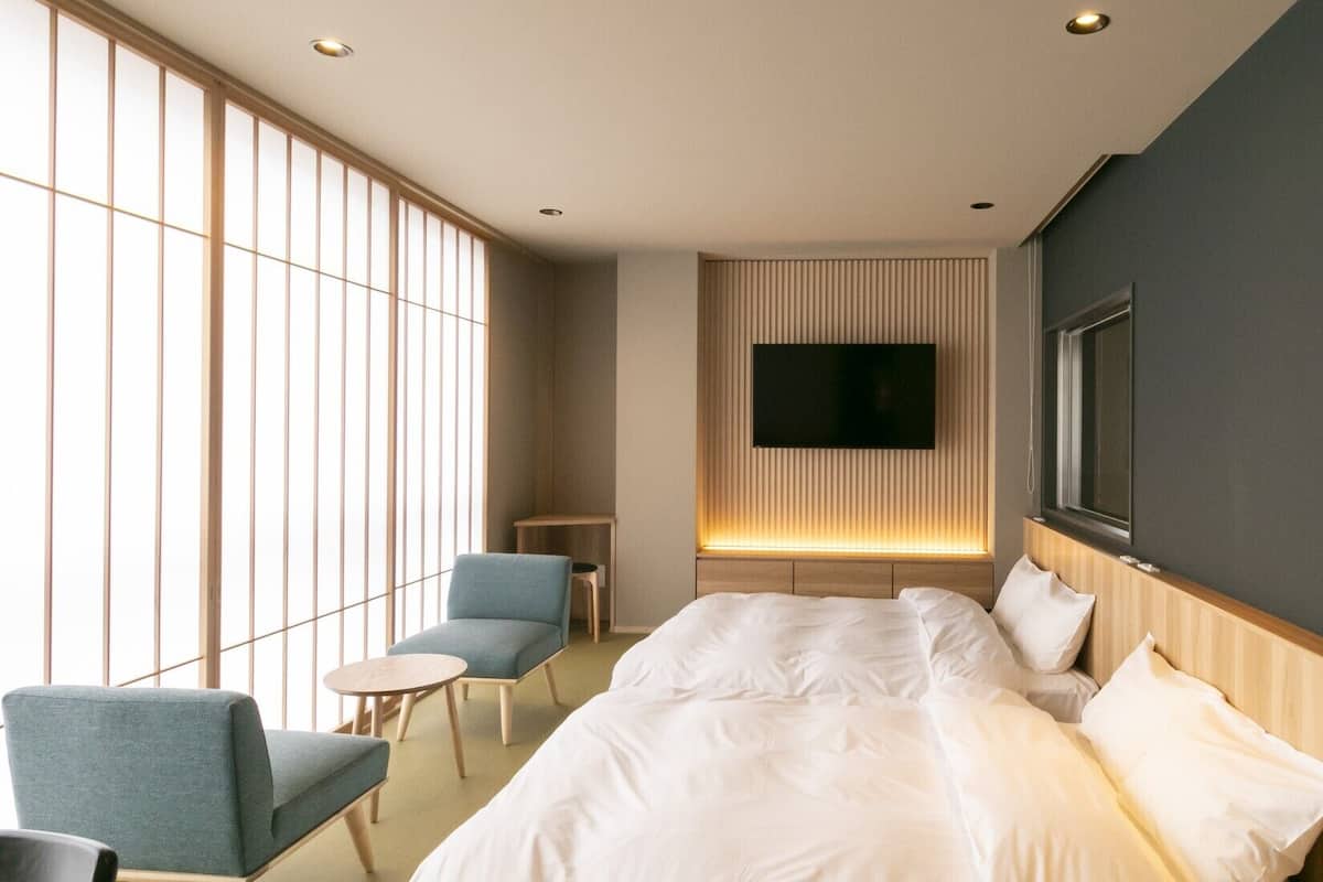 Hotellihuone, jossa on sänky, seinälle asennettu televisio, tuoli ja pieni pöytä.