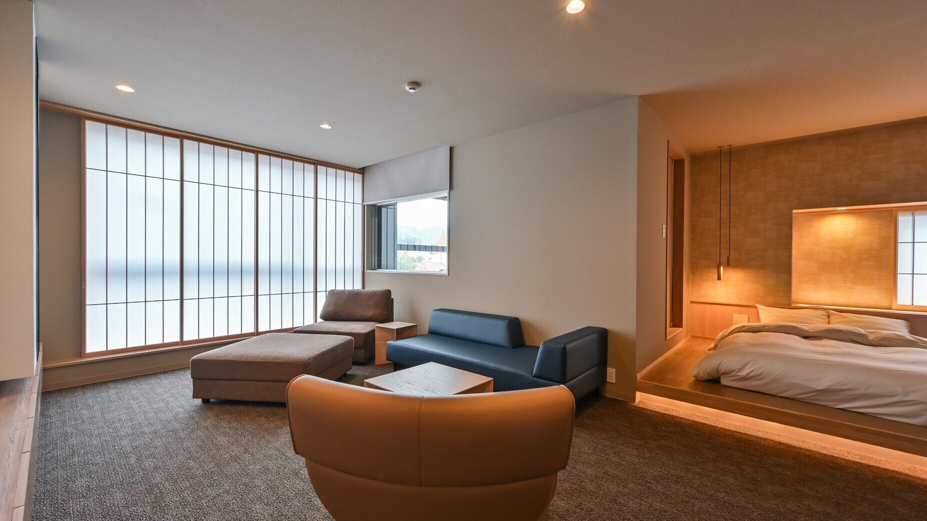 Ein modernes Hotelzimmer mit großem Fenster, einer Couch, einem Sessel, einem Bett und einem kleinen Tisch.
