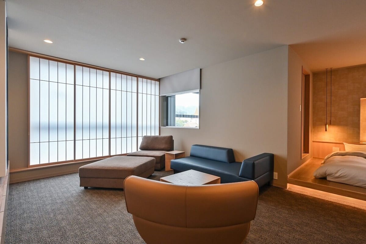 Moderni hotellihuone, jossa on suuri ikkuna, sohva, tuoli, sänky ja pieni pöytä.