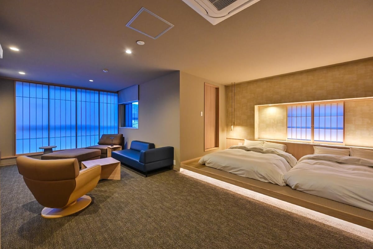 A modern hotel room with a large bed, a sofa, a small table, and a view of the sea through large windows.