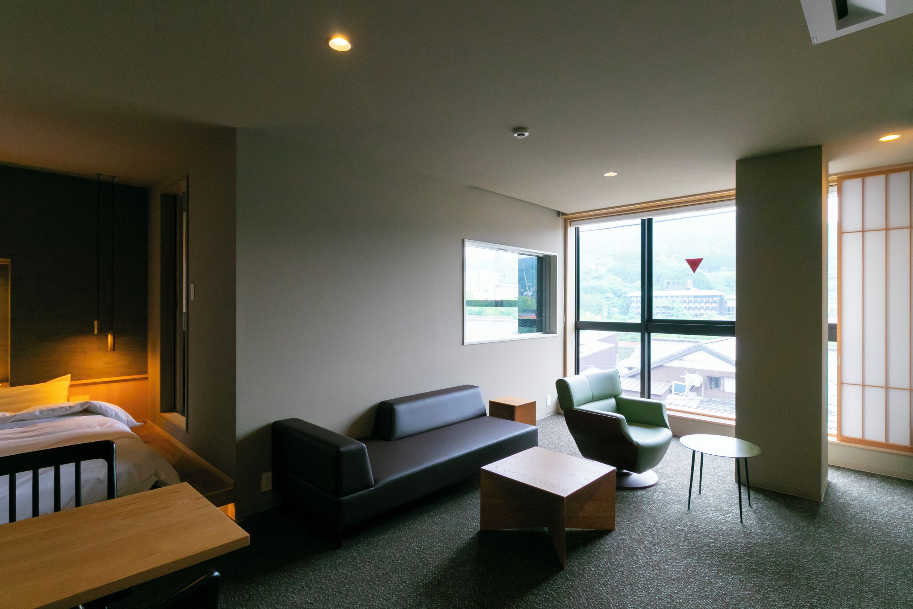 A modern hotel room with a bed, a sofa, a small table, and a window offering a city view.