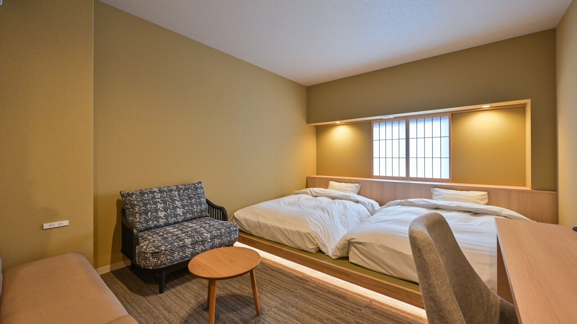 Ein Hotelzimmer mit zwei Betten, einem Sofa, einem kleinen Tisch und einem Fenster mit Jalousien.