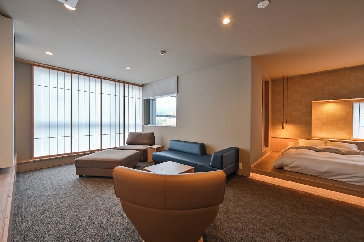 Moderni hotellihuone, jossa on suuri ikkuna, sohva, nojatuoli, sänky ja pieni pöytä.