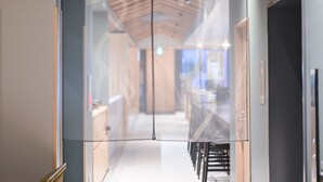 A modern interior with a glass partition, wooden ceiling beams, and a visible dining area with tables and chairs.