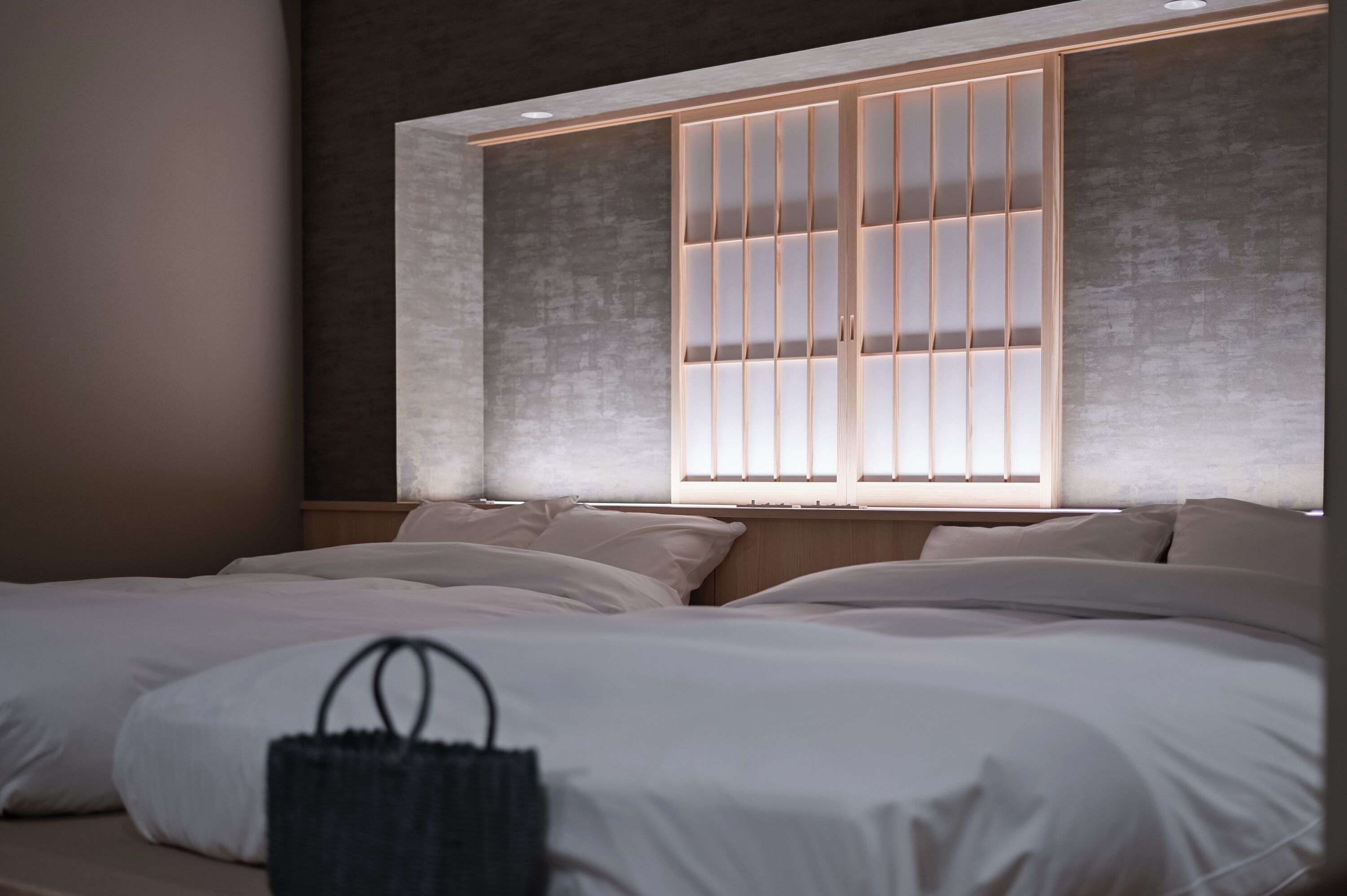 A modern bedroom with a large bed, a headboard with vertical slats, and a small black bag on the bed.