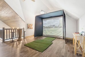 A room with a large window, a green artificial turf, a wooden desk, and a ceiling with exposed beams.
