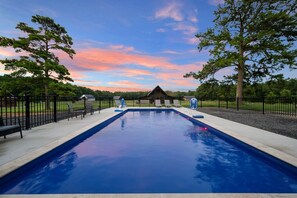 Una piscina rectangular con superficie de agua azul cristalina, rodeada por una cerca de metal negro, y un pabellón al fondo.