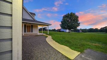 A residential house with a gravel driveway, a covered porch, and a large tree in the yard.