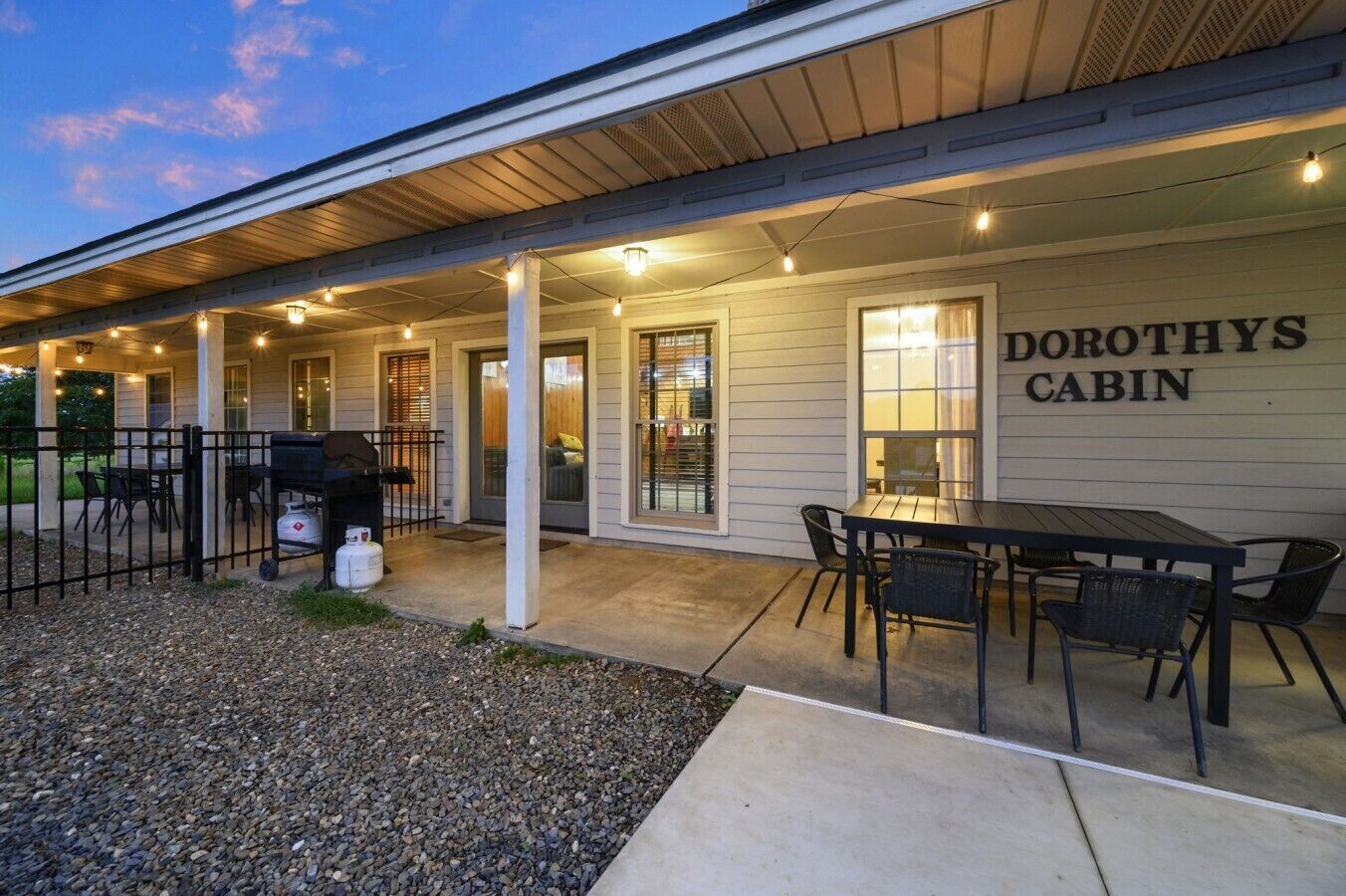 Un espace extérieur abrité, équipé d’une table et de chaises, d’un barbecue et d’une pancarte indiquant « CABANE DE DOROTHY ».