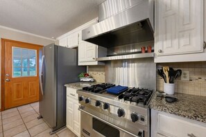 Una cucina con piano cottura in acciaio inossidabile, frigorifero ed elementi contenitori bianchi.