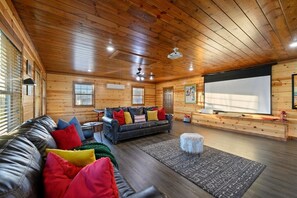 Un interior de cabaña acogedor con un sofá de cuero, un televisor y una pantalla de proyector.