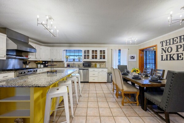 A modern kitchen with white cabinets, a granite countertop, and a dining area with a wooden table and chairs.