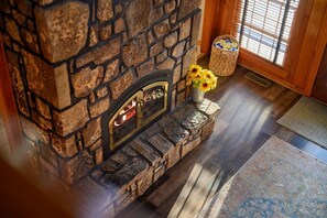 A stone fireplace with a fire, a rug, and a basket with flowers.