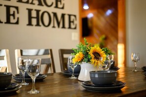 Una mesa de comedor dispuesta con platos, tazones y copas de vino, con un centro de girasoles.
