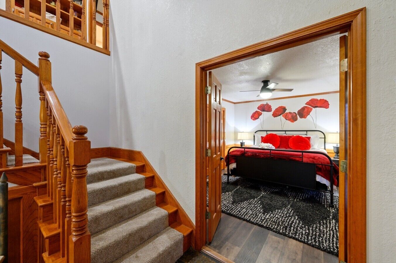 Ein Schlafzimmer mit einem Bett, einem roten und weißen Teppich, einer Holztreppe und einem Deckenventilator.