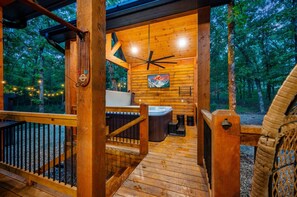 Eine Holzterrasse mit Whirlpool, Deckenventilator und Blick auf den Wald.
