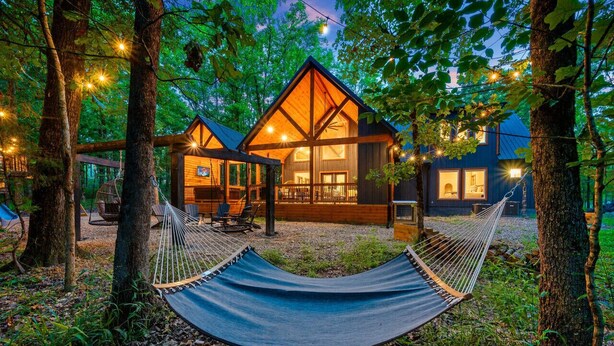 A cabin with a hammock, wooden deck, and string lights. - Hidden Gem · Boho Chic Paradise: Arcade & Fire Pit Swing Area (Broken Bow)