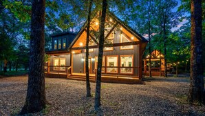 A cabin with a large deck, multiple windows, and a wooden exterior. - Hidden Gem · Boho Chic Paradise: Arcade & Fire Pit Swing Area (Broken Bow)