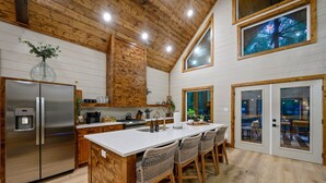 A kitchen with a central island, wooden cabinetry, and a stainless steel refrigerator. - Hidden Gem · Boho Chic Paradise: Arcade & Fire Pit Swing Area (Broken Bow)