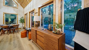 A wooden interior with a dining area, large windows, and a view of the outdoors. - Hidden Gem · Boho Chic Paradise: Arcade & Fire Pit Swing Area (Broken Bow)