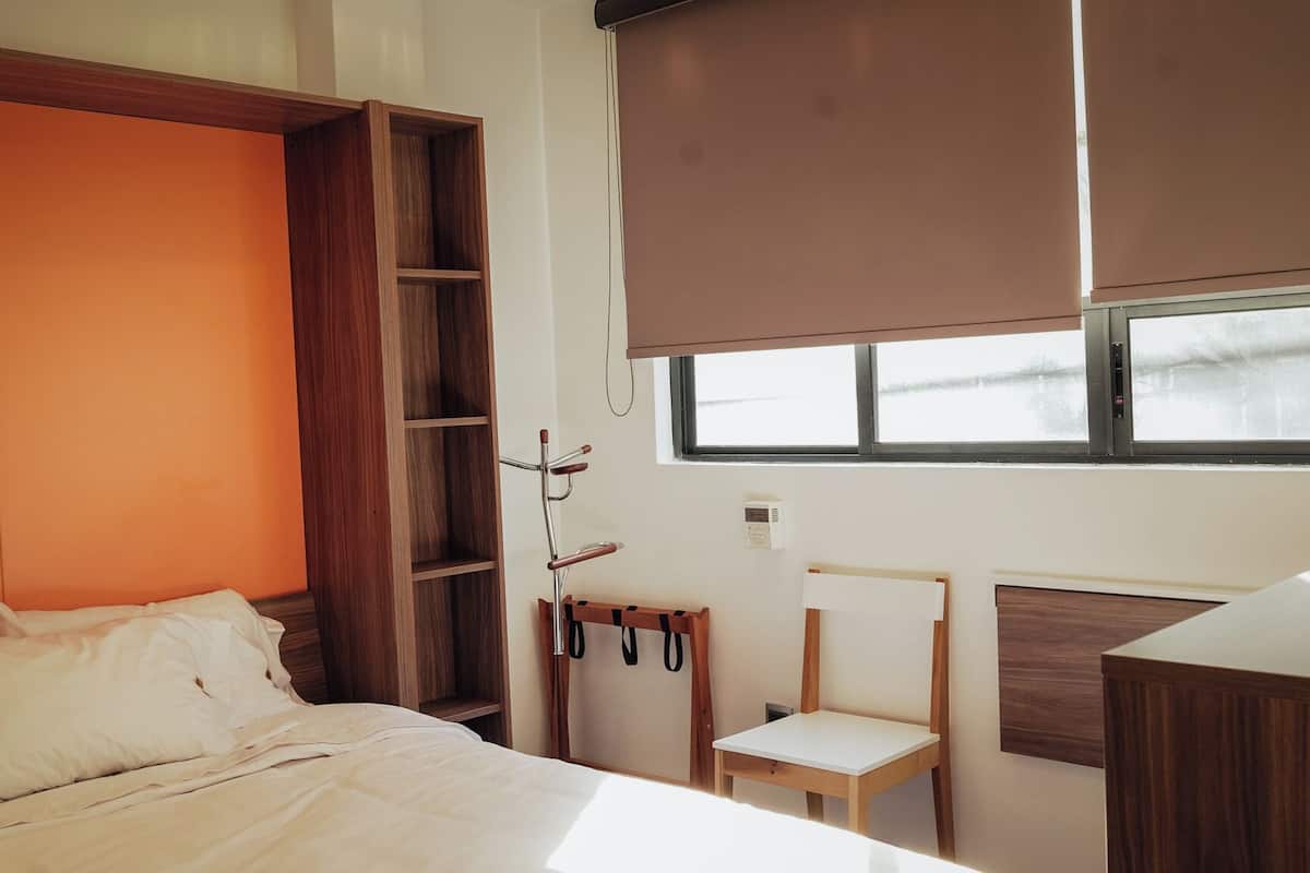 A bedroom with a bed, a wooden wardrobe, a small table, and a window.