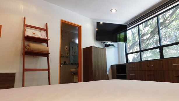 Un dormitorio con una cama grande, un televisor montado en la pared, un armario y una ventana con vistas a árboles.