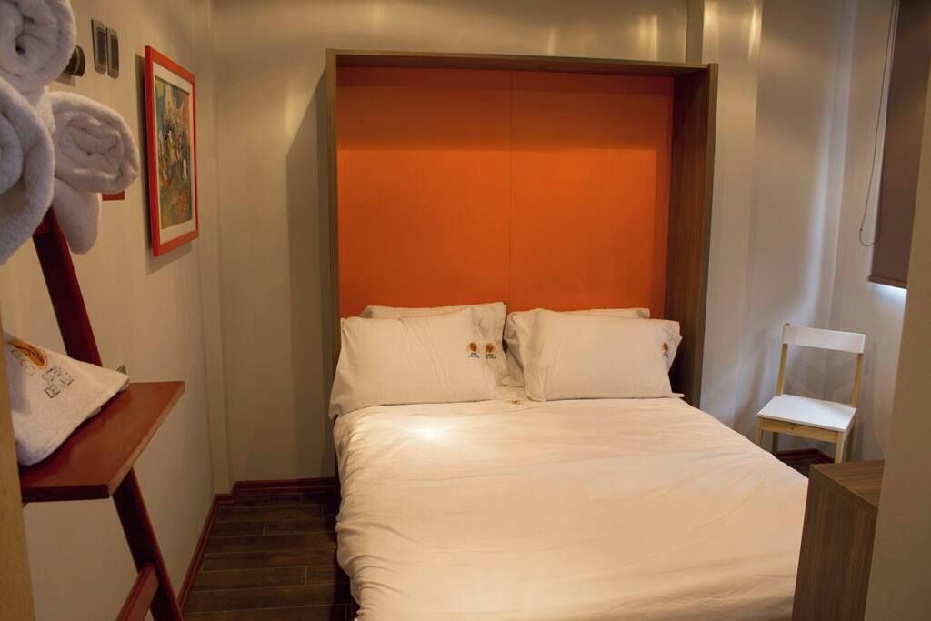Quarto de hotel com cama, uma cadeira, porta-toalhas e um quadro na parede.