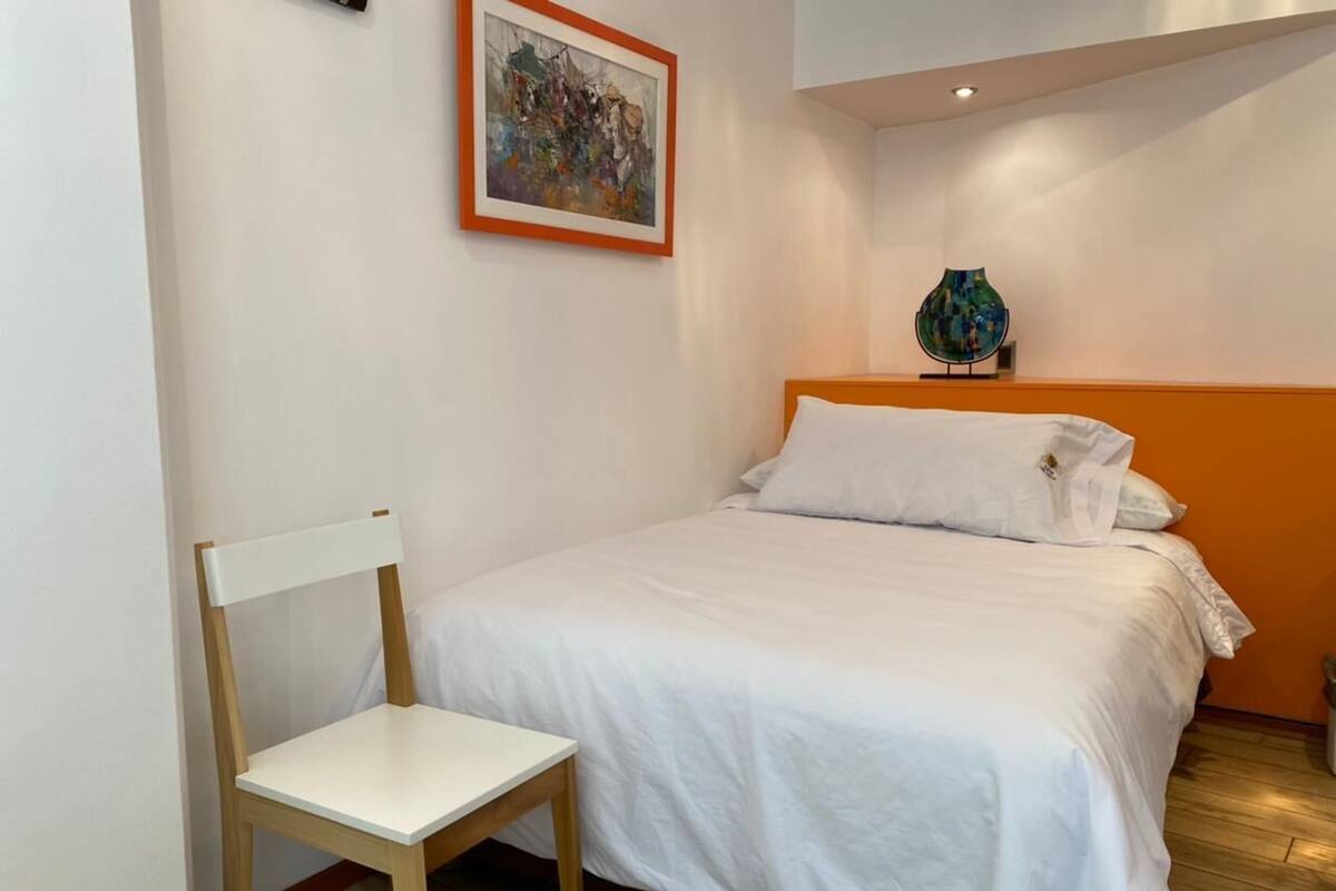 A bedroom with a bed, a chair, a painting, and a vase.