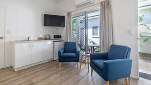 Una camera moderna con angolo cottura, due poltrone blu, un tavolino e una TV fissata al muro.