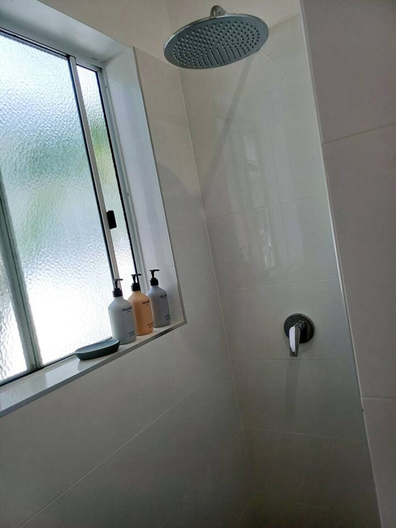 Une salle de bain avec une douche, une fenêtre et des articles de toilette rangés sur une étagère.