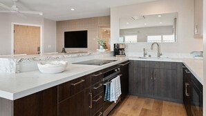 A modern kitchen with dark wood cabinets, a marble countertop, a built-in oven, and a large mirror above the sink.