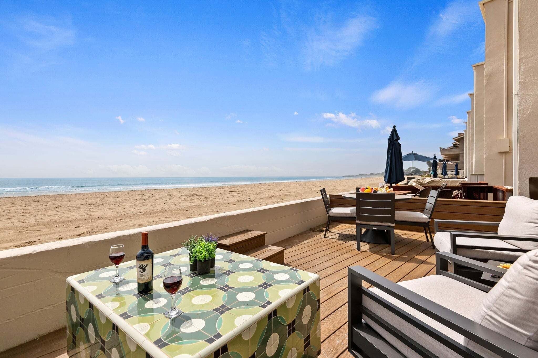 Une terrasse en bois avec une table, des chaises et une vue sur la plage.