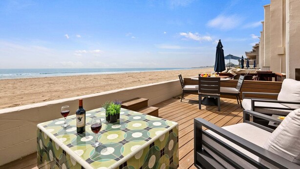 A wooden deck with a table, chairs, and a view of the beach.