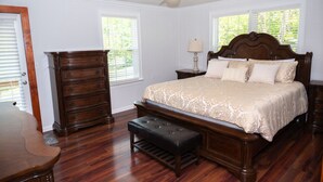 Quarto com cama de madeira, mesa de cabeceira, cômoda, banco e ventilador de teto.