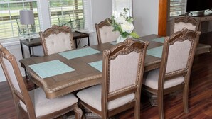 Uma sala de jantar com mesa e cadeiras de madeira, um lustre e um espelho grande.