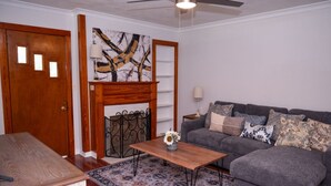 Uma sala de estar com um sofá cinzento, uma mesa de centro de madeira e um tapete estampado.