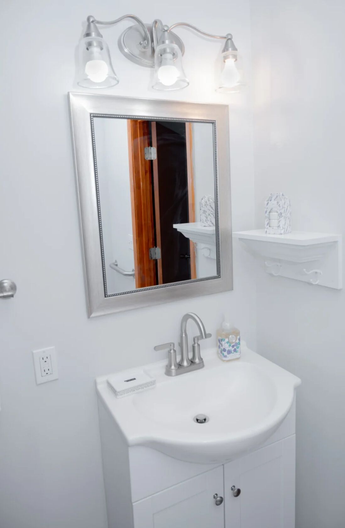 Une salle de bain avec un lavabo blanc, un miroir avec un cadre en bois et un luminaire placé au-dessus du miroir.
