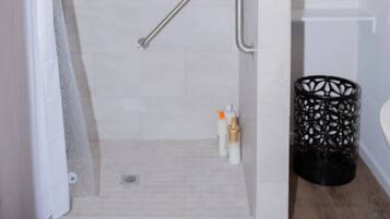 A modern shower area with a glass door, a handrail, and a showerhead.