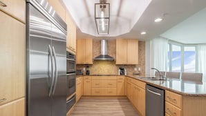 A modern kitchen with wooden cabinets, stainless steel appliances, a large island with a sink, and a view of the outdoors. - Modern 4 Bedroom Condo with Panoramic Views and Large Wraparound Balcony. Complimentary Boat Slip! (Orange Beach)