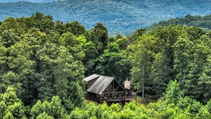 Uma cabana rodeada por floresta densa, com vista para as montanhas ao fundo.