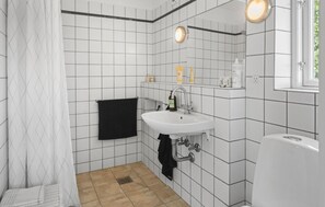 Une salle de bain avec des murs recouverts de carreaux blancs, un lavabo blanc et une serviette noire accrochée au mur.