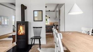 Un soggiorno moderno con stufa a legna, un'area pranzo con tavolo in legno e una cucina sullo sfondo.