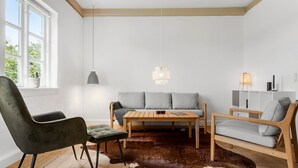Un soggiorno moderno con un tavolo in legno, due divani, una poltrona in pelle, un tappeto in pelle di vacca e una finestra con vista sul verde.