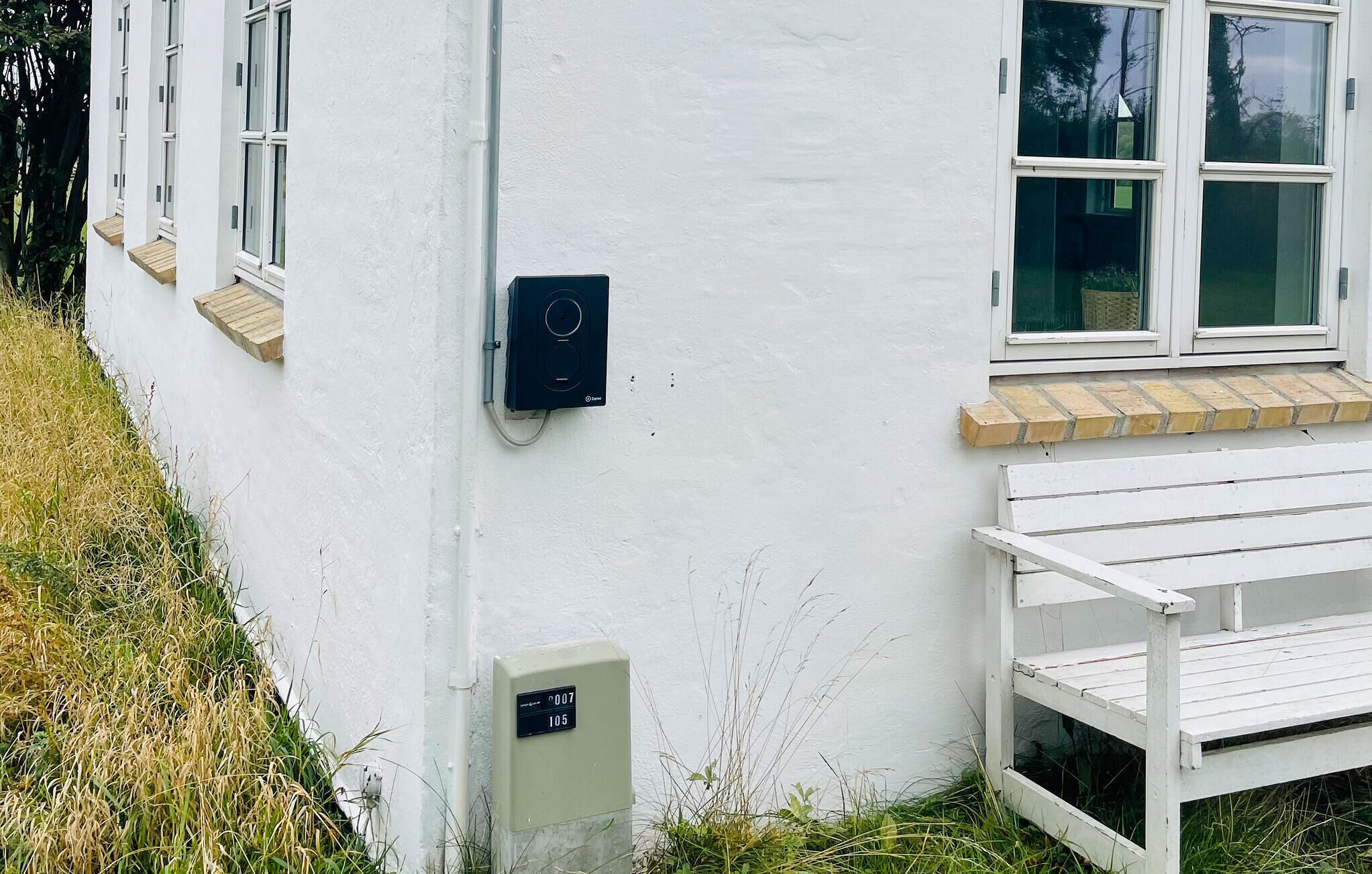 A white building with a window, a doorbell, and a small outdoor bench.