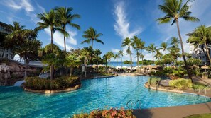 Relax by the pool surrounded by lush greenery and palm trees, with lounge chairs and umbrellas nearby.