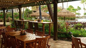 Enjoy meals and drinks under a shaded pergola surrounded by lush greenery and a serene pool view.