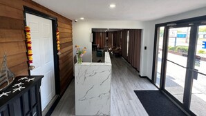 Eine Hotelhalle mit einer Rezeption, Holzvertäfelung, einer Marmorplatte und Blick auf die Straße durch große Glasschwingtüren.